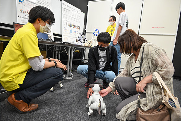 コミュニケーションロボットと触れ合った参加者からは「かわいいね」「歌ってくれたよ！」と感嘆の声が上がった（電気システム工学科）