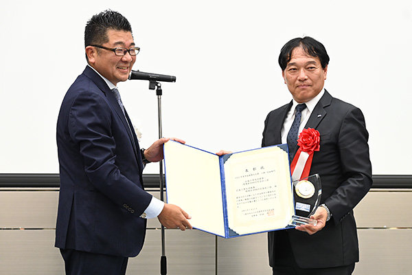 表彰式には同会会長の尾立道泰氏が登壇。表彰状とトロフィーが授与された