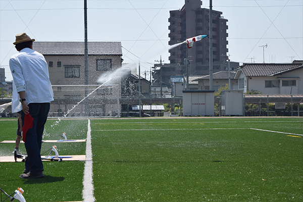 「ブシュッーーー！！」水と空気を噴射して、打ち上がるロケット。学生スタッフは空気入れ補助や飛距離測定でお手伝いします。