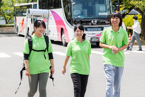 地球環境学科の女子学生たち。左の女子学生が背負っているのは周囲の温度・湿度・気圧が測れる測定装置。ヒートアイランド現象の研究などに使用するのですが、暑いこの日は広島工業大学を測定して回っていました。