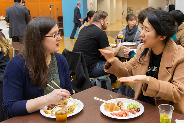 「広島の食べ物は何でもおいしいわね。お好み焼きもグッドだった。私が好きなカナダ料理にプーティンというのがあるんだけど、お礼にいつかごちそうしたいわ」と、本学学生とグルメの話で盛り上がるHannah Olneyさん（写真左）